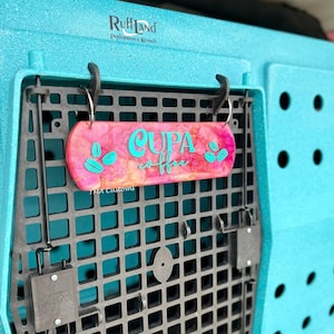 May include: A rectangular pink and orange marbled sign with the teal text "CUPA coffee" and teal coffee bean graphics, hanging from a black plastic grid on a textured teal kennel. The sign features the small white text "TMA Customs".