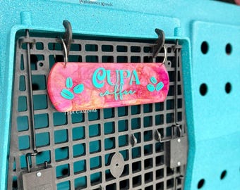 May include: A rectangular pink and orange marbled sign with the teal text "CUPA coffee" and teal coffee bean graphics, hanging from a black plastic grid on a textured teal kennel. The sign features the small white text "TMA Customs".