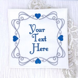 May include: White embroidered patch with a silver and blue frame and the text "Your Text Here" in the center.