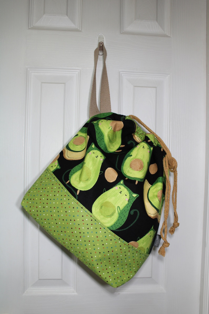 Puede incluir: Una bolsa de cord&oacute;n negro con un estampado de aguacate verde y marr&oacute;n. La bolsa tiene un fondo de lunares verde y marr&oacute;n y un cord&oacute;n de color marr&oacute;n.