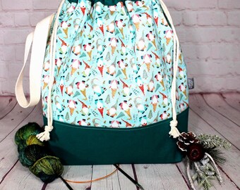 Puede incluir: Una bolsa de proyecto con cordón ajustable en tela azul claro con un patrón repetitivo de gnomos y pequeños pinos. La sección inferior es de color verde oscuro sólido y la bolsa incluye correas de cordón blanco grueso y un asa lateral.