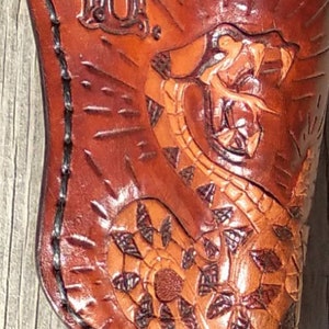 K&ouml;nnte beinhalten: Ein braunes Lederholster mit einem detaillierten Schlangendesign. Die Schlange ist in Orange- und Braunt&ouml;nen geschnitzt und gef&auml;rbt. Die Initialen "L.U." sind oben eingepr&auml;gt. Das Holster ist mit schwarzem Faden gen&auml;ht.