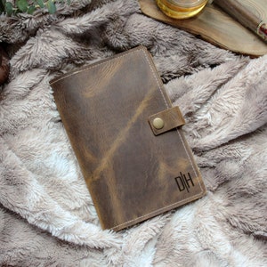 May include: A brown leather journal with a flap closure and a brass button. The journal has the initials "DH" embossed on the front.