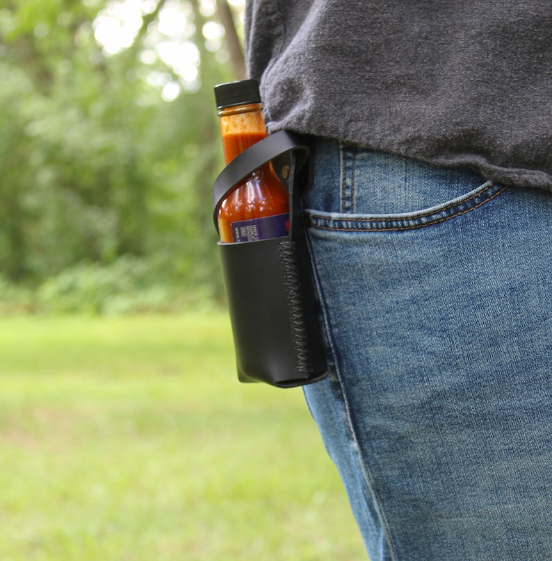 Peut inclure: Un porte-sauce piquant en cuir noir avec un design cousu. Le porte-sauce est attach&eacute; &agrave; une boucle de ceinture et contient une bouteille de sauce piquante.