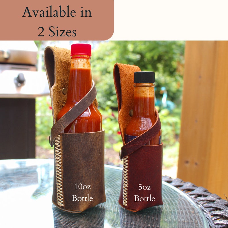 Peut inclure: Deux porte-bouteilles de sauce piquante en cuir avec des bouteilles de tailles diff&eacute;rentes. Le plus grand porte-bouteille est brun avec des coutures blanches et indique "10oz Bottle". Le plus petit porte-bouteille est brun et rouge avec des coutures blanches et indique "5oz Bottle".