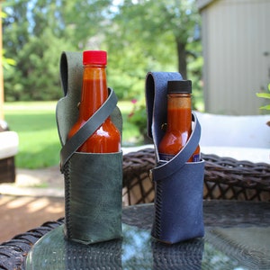 Peut inclure: Deux porte-bouteilles de sauce piquante en cuir avec des bouteilles de sauce piquante &agrave; l'int&eacute;rieur. Le porte-bouteille de gauche est vert et celui de droite est bleu.