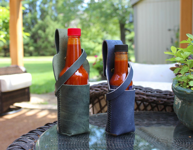 Peut inclure: Deux porte-bouteilles de sauce piquante en cuir avec des bouteilles de sauce piquante &agrave; l'int&eacute;rieur. Le porte-bouteille de gauche est vert et celui de droite est bleu.