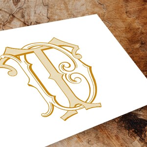 Op de afbeelding: Een gouden monogram met de letters "T" en "D" die in een decoratief, gestileerd lettertype met elkaar verweven zijn.