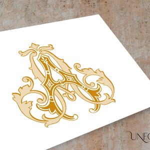 May include: A gold-coloured monogram featuring the letter "A" in a decorative, ornate font. The letter is surrounded by intricate floral designs.