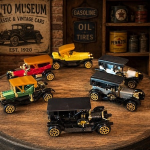 May include: A collection of miniature vintage car models in various colors, including red, yellow, green, and black, with gold-colored wheels. The cars are arranged on a wooden surface, with a Texaco gas pump and vintage signs in the background.