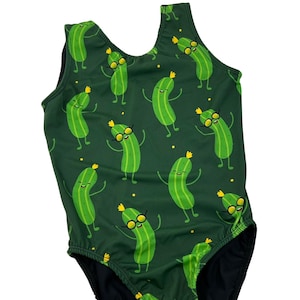 May include: A one-piece swimsuit with a dark green background and a repeating pattern of cartoon pickles. The pickles are green with yellow crowns and sunglasses, and are in various poses. The swimsuit has a black bottom.