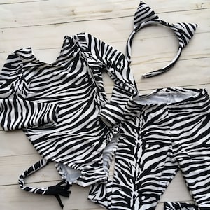 Może przedstawiać: Kostium zebry w czarno-białe pasy dla dziecka, w skład kt&oacute;rego wchodzi body z długim rękawem, legginsy, ogon i opaska na głowę z uszami.