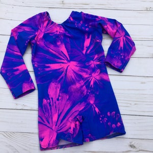 May include: A long-sleeved leotard with a blue background and a pink floral pattern. The leotard has a scoop neck and long sleeves.