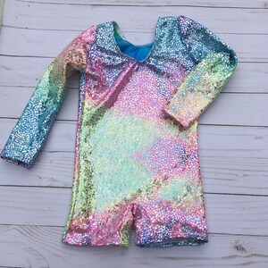 May include: A long-sleeved leotard with a rainbow iridescent pattern. The fabric has a textured, glittery finish.