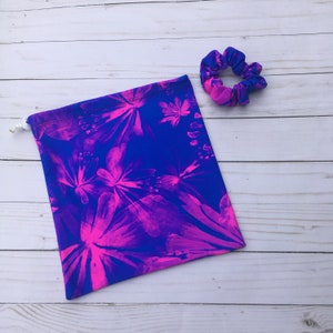 May include: A drawstring bag and scrunchie set. The bag and scrunchie feature a vibrant floral pattern in shades of blue and pink. The bag is rectangular with a white drawstring closure. The scrunchie is round and made of the same patterned fabric.
