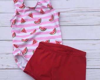 May include: A two-piece swimsuit set featuring a watermelon theme. The one-piece swimsuit has a pink and white striped pattern with watermelon slices. The matching shorts are solid red. The set is designed for children.