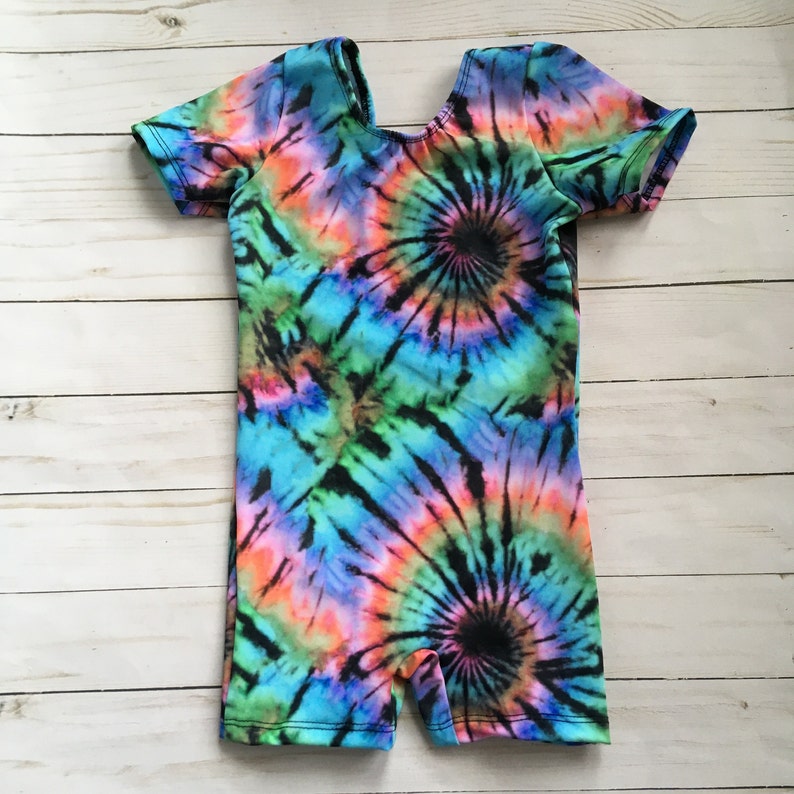 K&ouml;nnte beinhalten: Ein Batik-Leotard mit kurzen &Auml;rmeln und einem U-Boot-Ausschnitt. Der Leotard ist aus einem dehnbaren, bequemen Stoff gefertigt und hat ein lebendiges Wirbelmuster in Blaut&ouml;nen, Gr&uuml;n, Pink und Schwarz.