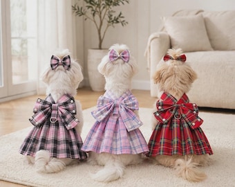 Pode incluir: Três cães pequenos vistos por trás, cada um vestindo um vestido xadrez com um grande laço nas costas adornado com pérolas brancas e um laço de cabelo a condizer. Os vestidos apresentam uma saia plissada e um anel em D, em preto e rosa, rosa claro, e vermelho e verde.