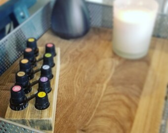 May include: A wooden tray with a row of ten small glass bottles with colourful lids. The bottles are arranged in a diagonal line. A black ceramic vase and a white candle are in the background.