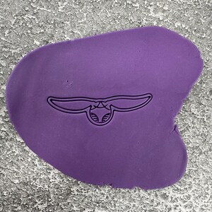 Könnte beinhalten: Lilafarbener Fondant mit einem Ausschnitt einer stilisierten Mantarochen, eine Art Rochen mit flügelartigen Brustflossen.