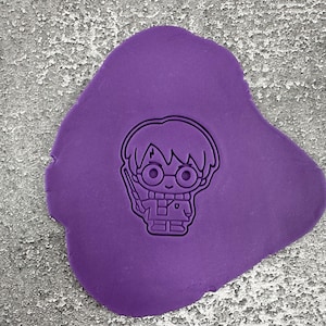 Könnte beinhalten: Lilafarbener Knetmasse mit der Umrandung eines Comic-Charakters mit Brille und einem Blitz auf der Stirn. Der Charakter hält einen Zauberstab.