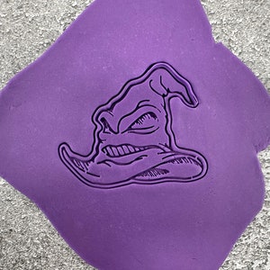 Könnte beinhalten: Eine lilafarbene Silikonform mit einem detaillierten Abdruck eines Zaubererhutes mit einem missmutigen Gesicht.