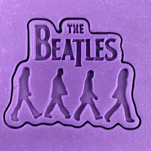 May include: Purple silicone mould with the text "The Beatles" and four walking figures in silhouette.