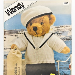 May include: A knitting pattern for a teddy bear dressed as a sailor. The pattern is called "Bear Necessities" and is from Wendy. The bear is wearing a white sailor shirt with a blue collar, blue pants, and a white sailor hat. The bear is holding a brown bag that says "HMS Teddy Bear".