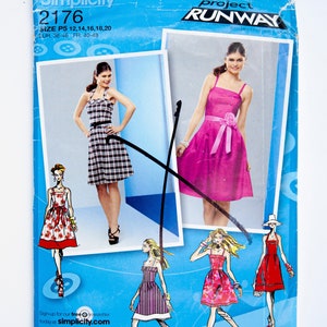 Op de afbeelding: Simplicity naaipatroon nummer 2176 voor een jurk, geïnspireerd door Project Runway. Het patroon omvat de maten P5 12, 14, 16, 18, 20, EUR 38-46, FR 40-48. Het patroon toont een model in een geruite jurk en een lijntekening van een model in een roze jurk met een strik.