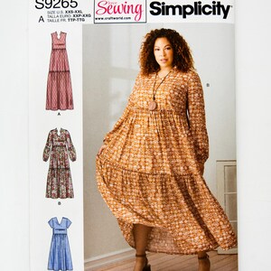 May include: Simplicity sewing pattern S9265 featuring three dress designs. The pattern includes sizes XXS-XXL. The main image shows a woman wearing a long-sleeved, tiered dress in a warm, patterned fabric. The pattern's logo and size information are visible.