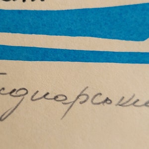May include: Artwork with blue brushstrokes and handwritten text. The text appears to be a signature in black ink. The background is a light beige color.