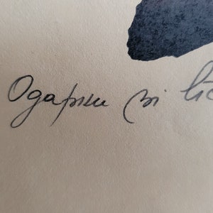 May include: Close-up of a handwritten script in black ink on a cream-colored paper. The script appears to be in a cursive style, with the text partially visible. The image also features dark blue ink blotches.