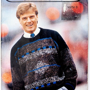 May include: A magazine cover featuring a man wearing a grey and blue patterned jumper. The magazine is titled "Novita of Finland" and the issue number is "No/Nr 8". The model is smiling and has his hand in his pocket. The magazine cover also includes the text "5342 Cashmere".