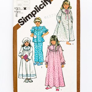 Peut inclure: Enveloppe de patron de couture Simplicity avec des illustrations de filles en chemises de nuit et pyjamas. L'enveloppe est marron et blanche, avec le logo Simplicity et des informations de prix. Les chemises de nuit sont blanches et roses, et les pyjamas sont bleus.
