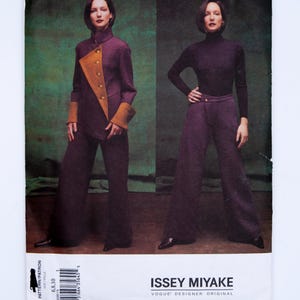 May include: A sewing pattern envelope for an Issey Miyake Vogue Designer Original. The front shows two outfits: a purple jacket with tan lapels and cuffs, and a purple turtleneck with matching wide-leg trousers. Text includes Issey Miyake.