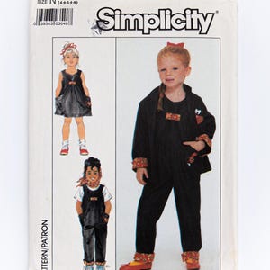 Puede incluir: Patrón de costura Simplicity número 8465 para la talla N (4+6+6). El patrón incluye tres atuendos para niños: un vestido negro con bolsillos, un mono negro con un lazo rojo y un mono negro con ribete estampado rojo y blanco.