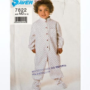 Pode incluir: Um padrão de costura vintage para um macacão infantil. O padrão mostra uma criança usando o macacão, que é branco com um pequeno padrão floral vermelho. O padrão está rotulado como "7822" e "SIZE MD (2-3)". O texto "NO EXCHANGE OR REFUND ON PATTERNS" também é visível.