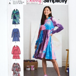 Puede incluir: Patrón de costura Simplicity S9380 con un vestido tie-dye. El patrón incluye varios estilos de vestidos, tallas XS-XL. La imagen muestra a una mujer con un vestido tie-dye en tonos morado, azul y rosa.