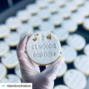 May include: A white round cookie with gold accents and the text "Elwoods Baptism" in white lettering.