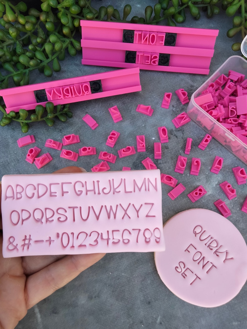 May include: Pink alphabet stamps in a clear plastic container. The stamps are arranged in a grid pattern. The stamps are made of a soft, flexible material. The stamps are used to create custom lettering on cakes, cookies, and other baked goods. The stamps are also used to create personalized gifts and decorations. The stamps are easy to use and clean. The stamps are a great way to add a personal touch to your baking and crafting projects.