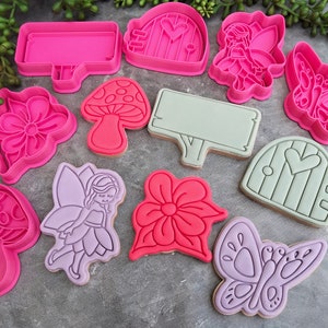 May include: A set of 10 pink, green, and purple cookie cutters shaped like mushrooms, flowers, butterflies, fairies, and doors. The cutters are made of plastic and are designed for making cookies.
