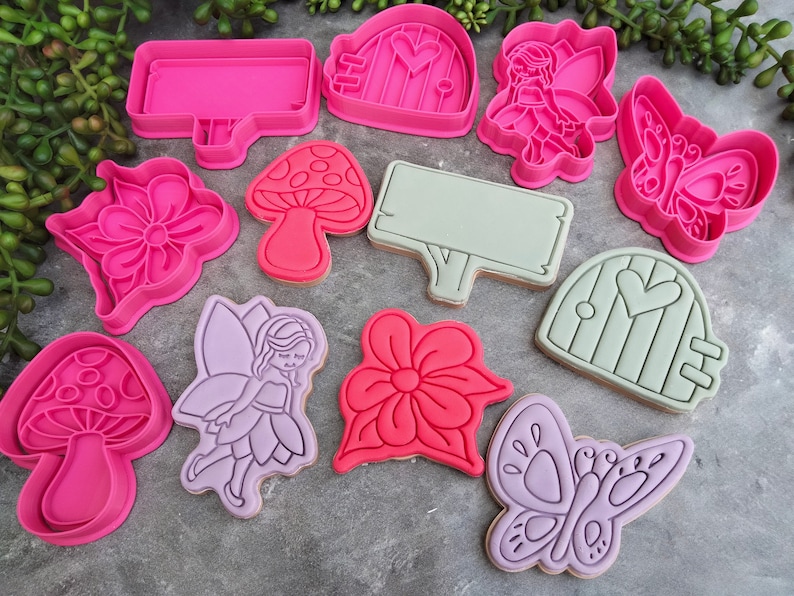 Op de afbeelding: Een set van 10 roze, groene en paarse koekjesvormen in de vorm van paddenstoelen, bloemen, vlinders, fee&euml;n en deuren. De vormen zijn gemaakt van plastic en zijn ontworpen voor het maken van koekjes.
