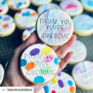 May include: A close-up of two decorated sugar cookies. One cookie has a white background with colorful polka dots and the text "Thank You You're Awesome". The other cookie has a white background with a pink and blue marbled design and the text "Thank You You're Awesome".