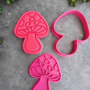 Op de afbeelding: Twee roze plastic koekjesvormen in de vorm van een paddenstoel. E&eacute;n vorm is massief en de andere is een omtrek.