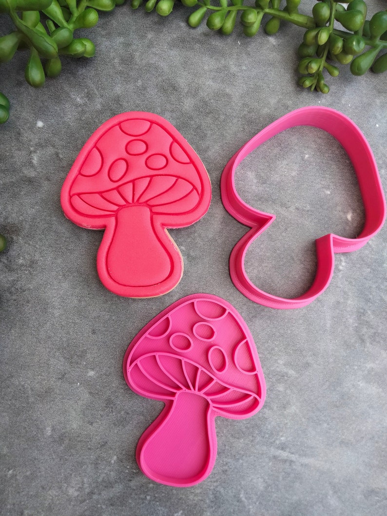 Op de afbeelding: Twee roze plastic koekjesvormen in de vorm van een paddenstoel. E&eacute;n vorm is massief en de andere is een omtrek.