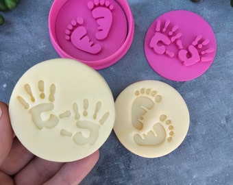 May include: Two pink silicone cookie cutters, one with a pair of footprints and the other with a pair of handprints. Two yellow silicone mats with impressions of the cookie cutters.