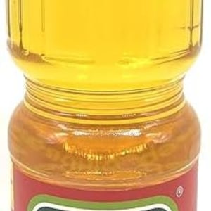 May include: A clear plastic bottle filled with yellow liquid, likely cooking oil. The bottle has a red cap and a label with green and white text and a sunflower illustration. The text "Schedryi Dar" is visible on the label.