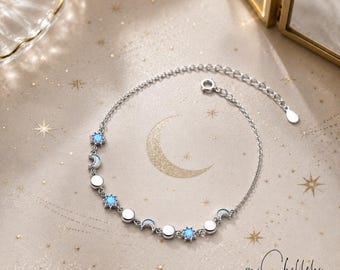 May include: A silver-toned chain bracelet featuring alternating charms of glowing blue stars, crescent moons, and small circular discs. The bracelet includes a delicate link chain with a circular clasp and an adjustable extension chain.