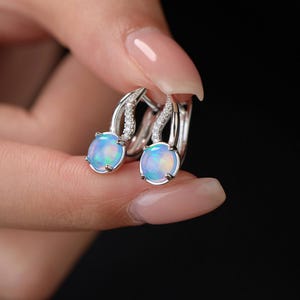 May include: Silver hoop earrings featuring a light blue opal stone and small clear crystals. The earrings are shown against a dark backdrop. The text "MICHELLELEE STUDIO Handcrafted Jewellery" is at the bottom.