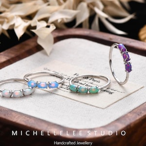 Könnte beinhalten: Vier silberne Ringe, jeder mit drei kleinen ovalen Steinen in den Farben Weiß, Hellblau, Grün und Violett. Die Ringe sind auf einer kleinen rechteckigen Karte mit dem Text MICHELLELEE STUDIO Handcrafted Jewellery angeordnet.